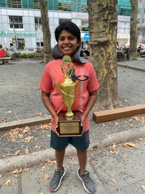 A student smiling with a large chess trophy